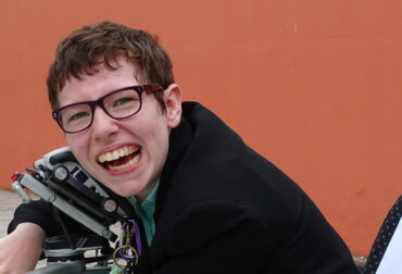 Beth Moulam and lifelong learning. Woman in wheelchair, hugging communication aid, AAC