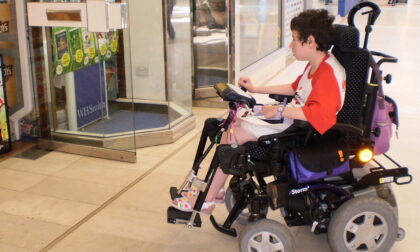 Young woman with cerebral palsy in power wheelchair entering a shop