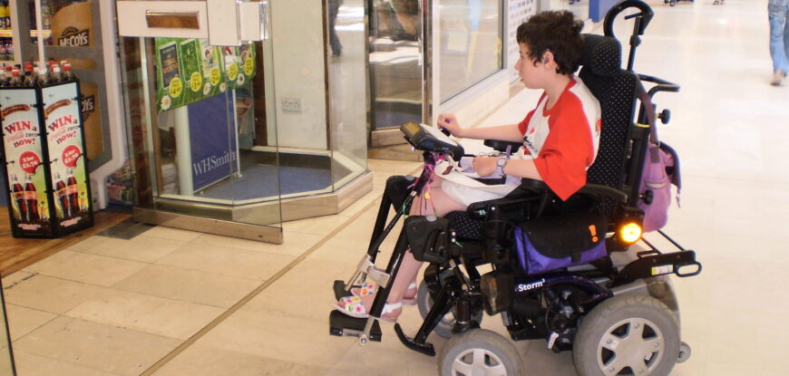 Young woman with cerebral palsy in power wheelchair entering a shop