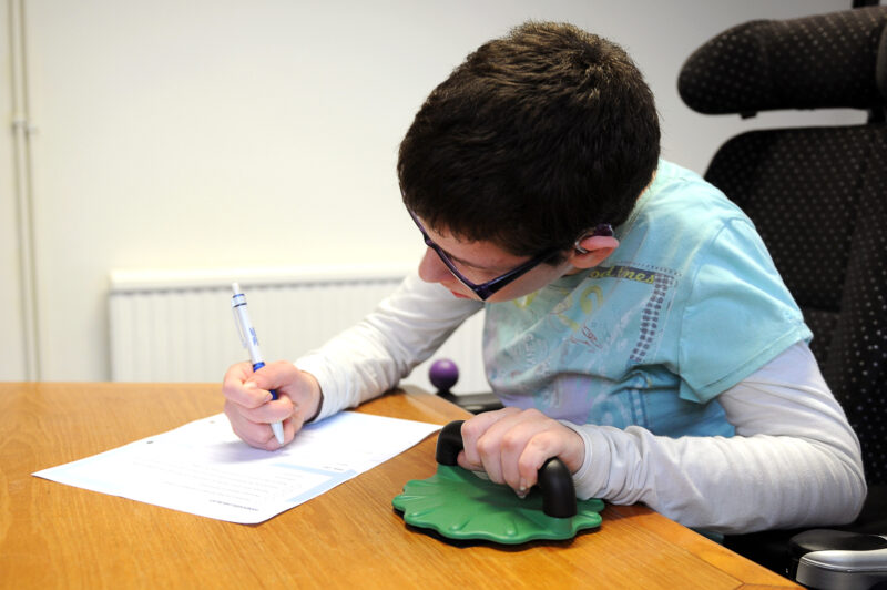 Beth Moulam, Girl with cerebral palsy wearing turquoise and white t shirt, holding pencil to write. stabilising with hand grip.