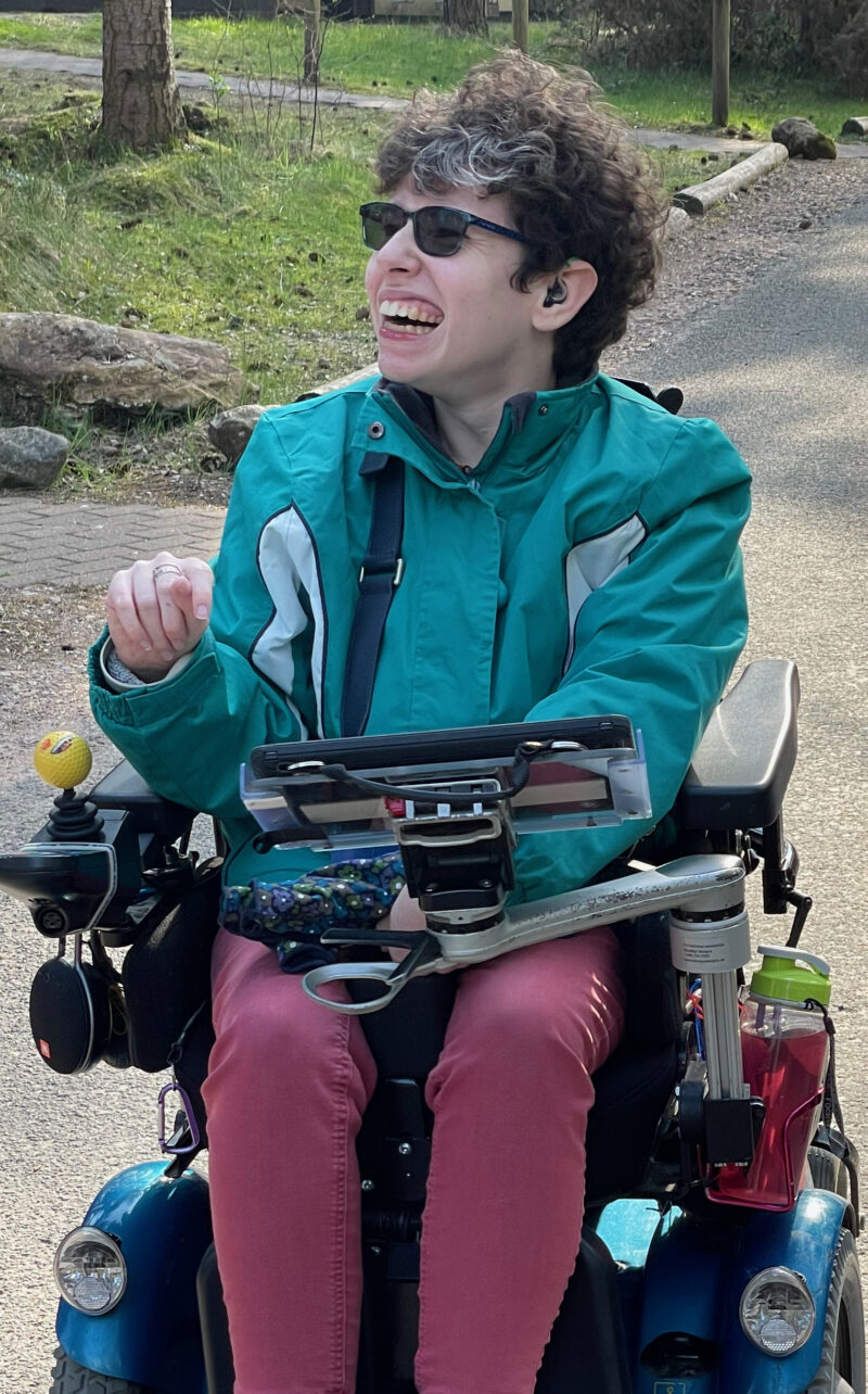 Beth Moulam, woman with Cerebral Palsy in power wheelchair and using communication aid. OUtside enjoying fresh air.