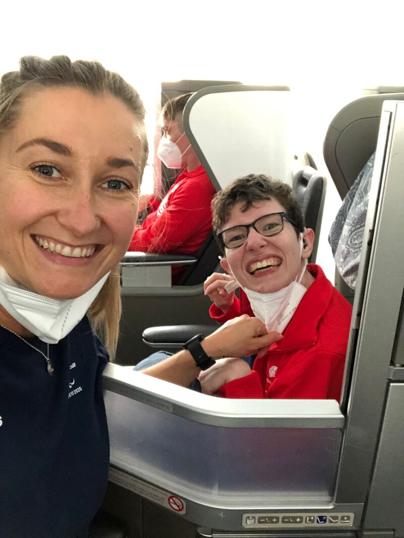Beth Moulam, female with Cerebral Palsy and assistant on British Airways flight to Tokyo 2020, sat in business class wearing red and navy kit and around necks covid masks.