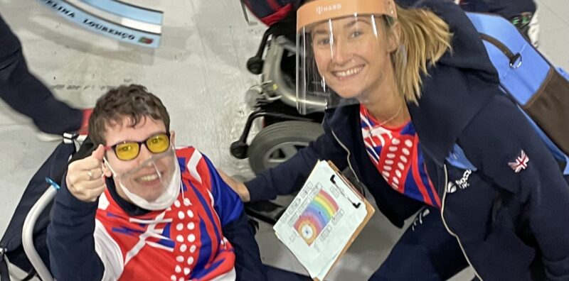 Beth Moulam BC3 boccia athlete and Christie Hutchings Ramp Operator. Wearing sports kit and clear lip reading masks. Beth with thumbs up, showing delight qualified for the BC3 individual semi-finals.