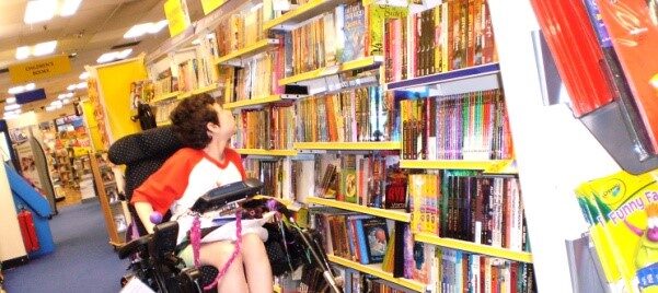 Beth Moulam, girl in red and white t shirt, looking at books sat in wheelchair, world book day