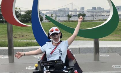 Beth Moulam, boccia athlete, in Tokyo 2020 Paralympic Games athlete village in front of the agitos logo. Wearing pale blue GB kit, hat and sunglasses on head. Reflections on stepping back from boccia