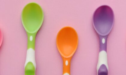 AAC spoons and speech fatigue. 5 coloured plastic spoons in pink, green, orange, purple and red on a pink background as a visual for spoon theory