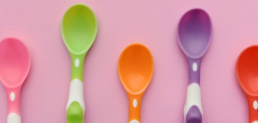 AAC spoons and speech fatigue. 5 coloured plastic spoons in pink, green, orange, purple and red on a pink background as a visual for spoon theory