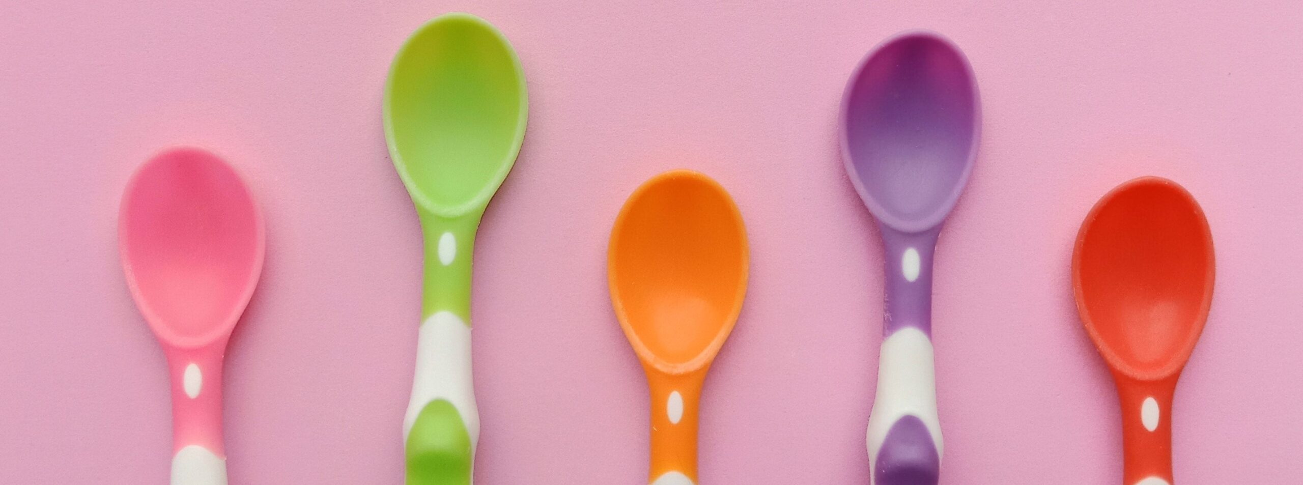 AAC spoons and speech fatigue. 5 coloured plastic spoons in pink, green, orange, purple and red on a pink background as a visual for spoon theory