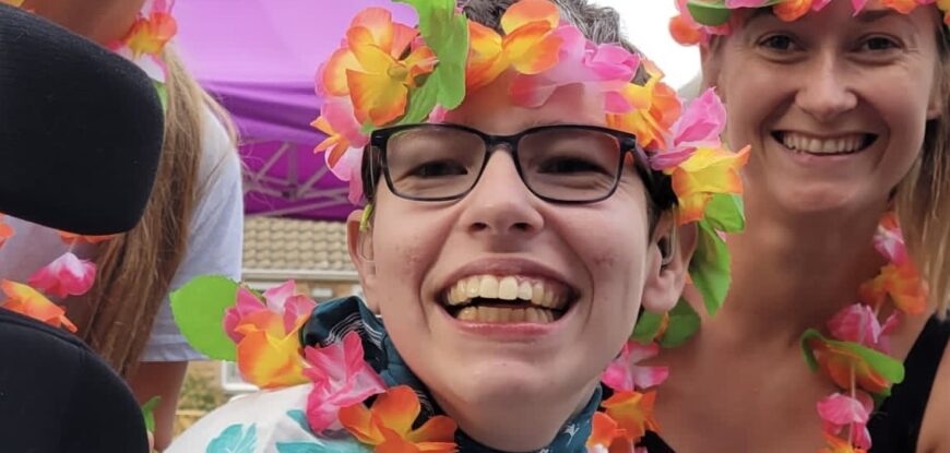 Beth Moulam and support team. AAC user and self advocate, Woman wearing glasses and flower headband and neck garland.