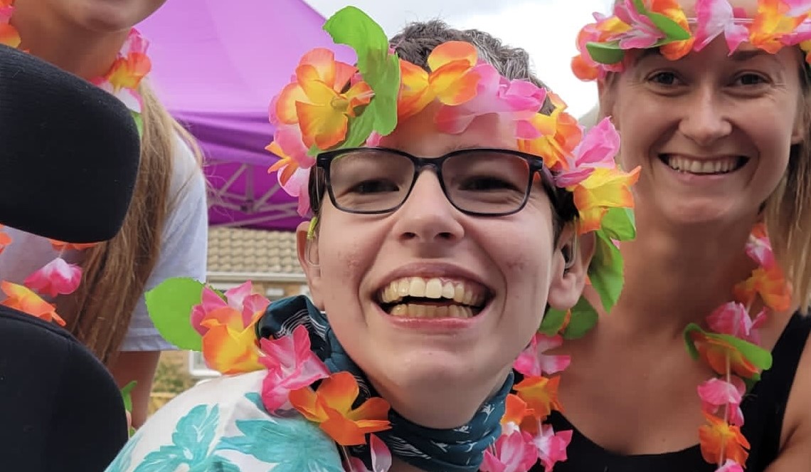 Beth Moulam and support team. AAC user and self advocate, Woman wearing glasses and flower headband and neck garland.