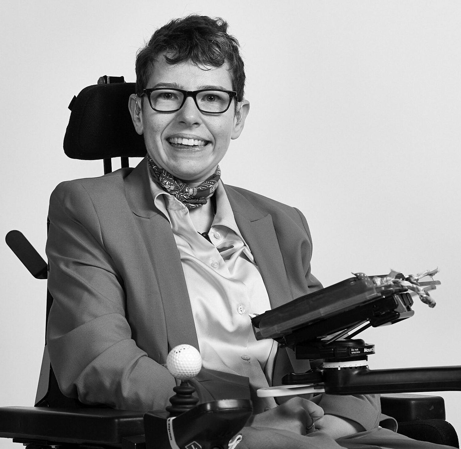 Beth Moulam Black and white photo sat in power chair with communication aid AAC device. Shaw Trust Disability Power 100 2023 Community Advocate